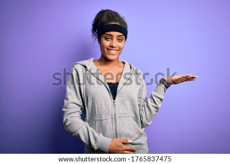 Young african american sportswoman doing sport wearing sportswear over purple background smiling cheerful presenting and pointing with palm of hand looking at the camera.