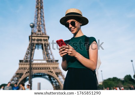 Caucasian woman browsing wireless network during time for romantic French walk in Paris, carefree female tourist enjoying smartphone communication standing at street with Eiffel Tower on background
