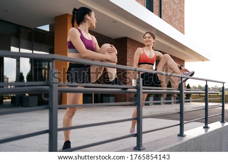 Athlete women preparing for, running on the city street. Legs warming and stretching. Sport tight clothes. Horizontal. 30s