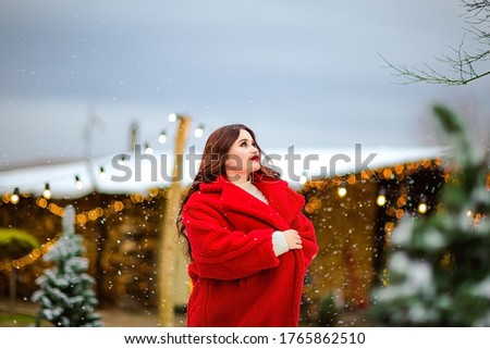 Young pretty long haired brunette woman in red long coat skating at the open skating rink. Christmas background.