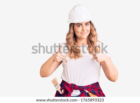 Young caucasian woman wearing security helmet success sign doing positive gesture with hand, thumbs up smiling and happy. cheerful expression and winner gesture. 