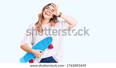 Young caucasian woman holding skate smiling happy doing ok sign with hand on eye looking through fingers 