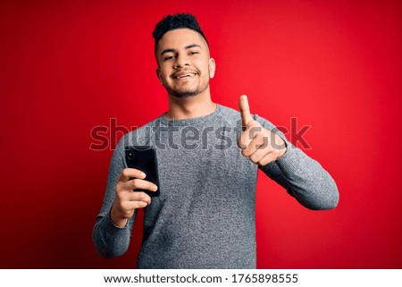 Young handsome man having conversation using smartphone over red background happy with big smile doing ok sign, thumb up with fingers, excellent sign