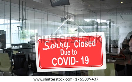 A sign reading closed due to the COVID-19 pandemic outbreak hangs on the glass window of a cafe or Business office.