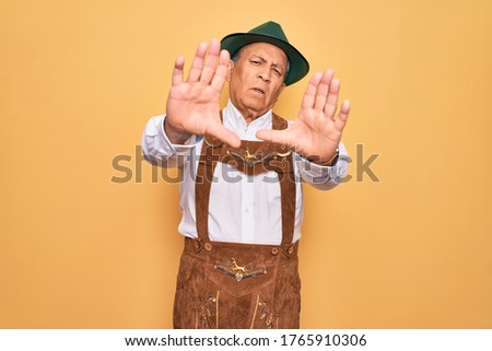 Senior grey-haired man wearing german traditional octoberfest suit over yellow background doing frame using hands palms and fingers, camera perspective