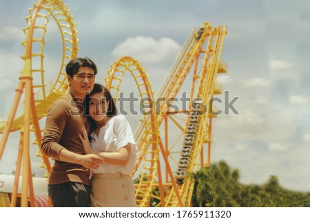 Asian couples make an appointment to visit an amusement park : Portrait young couple hugged in love in an amusement park on a clear day.
