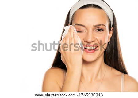 young smiling woman cleaning her face withwet tissue on white background Royalty-Free Stock Photo #1765930913