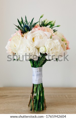 bridal bouquet of white and pink peonies, eryngium and green buds, with white ribbons on the table