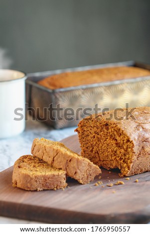 Fresh baked homemade pumpkin bread over a cutting board with steaming hot coffee in background. 