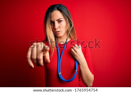Young beautiful brunette woman using stethoscope standing over isolated red background pointing with finger to the camera and to you, hand sign, positive and confident gesture from the front