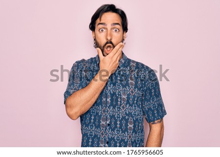Young handsome hispanic bohemian man wearing hippie style over pink background Looking fascinated with disbelief, surprise and amazed expression with hands on chin