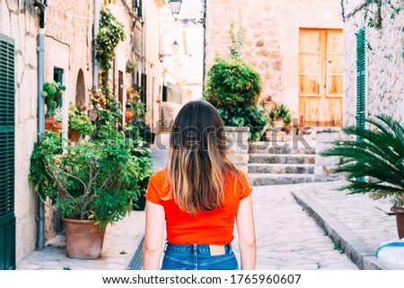 A Long-haired person exploring rural areas in Mallorca with red backpack and striped hipster shirt.