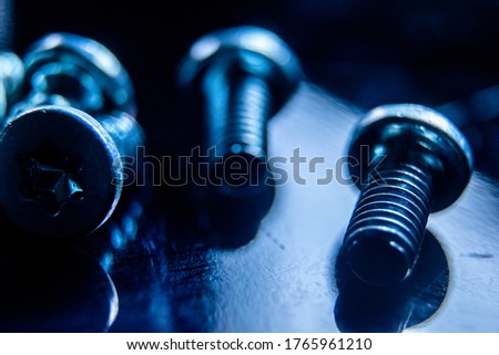 A closeup of a computer metal silver screws under blue lights on a dark shiny background