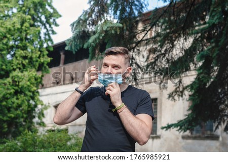 Handsome man incorrectly puts on a medical face mask. A man puts on a disposable mask under his nose. Royalty-Free Stock Photo #1765985921