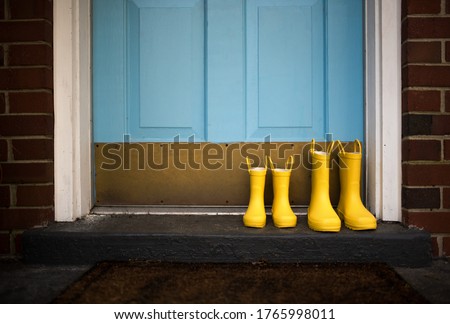Yellow rain boots sitting on front stoop in front of a blue door Royalty-Free Stock Photo #1765998011