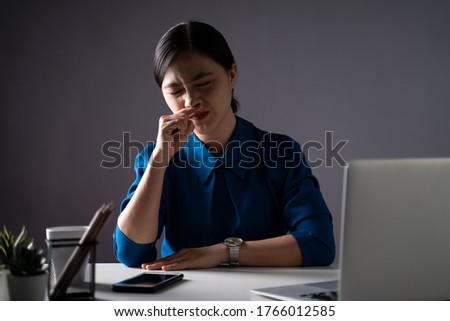 Asian woman in blue shirt was sick with fever, working on a laptop at office. isolated on white background. Low key.