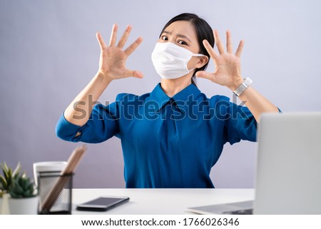 Don't Touch Your Face. Asian woman in blue shirt wearing protective face mask, showing hand making stop sign, working on a laptop sitting at office. isolated on white background.