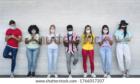 Young people wearing face mask using mobile smartphone outdoor - Multiracial friends having fun with new technology social media app during corona virus outbreak - Youth millennial lifestyle concept Royalty-Free Stock Photo #1766057207