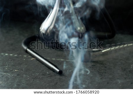 The hookah stands on the table on a black background. There is smoke