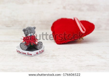 Miniature teddy bear and red heart on gray wooden background