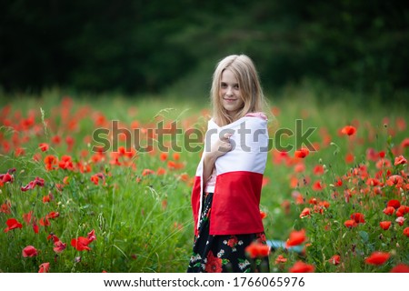 Blond girl wrapped in flag of Poland in the poppy field. Polish Flag Day. Travel and learn polish language concept. Royalty-Free Stock Photo #1766065976
