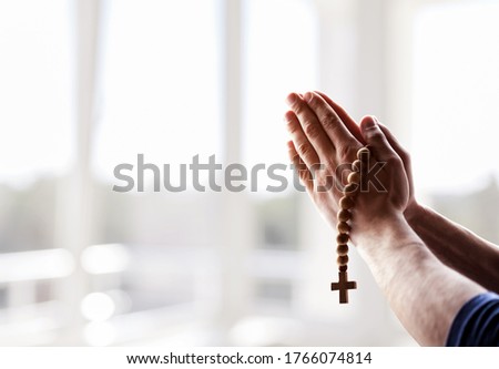 Religious christian man praying with rosary beads