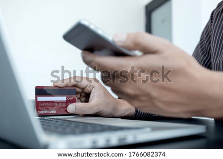 The businessman's hand is holding a credit card and using a smartphone for online shopping and internet payment in the office.