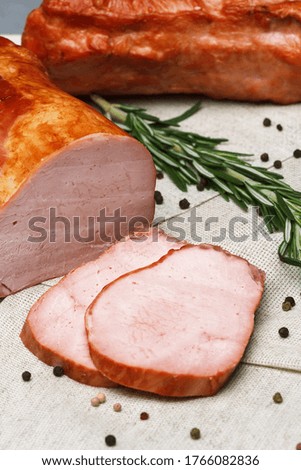 Sliced smoked ham lying on a rustic linen cloth, complete with black pepper and a branch of rosemary. A natural organic farm product produced using traditional methods.