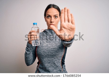 Young fitness woman wearing sport workout clothes drinking water from plastic bottle with open hand doing stop sign with serious and confident expression, defense gesture