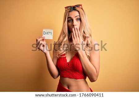 Beautiful blonde slim woman on vacation wearing bikini holding reminder with diet message cover mouth with hand shocked with shame for mistake, expression of fear, scared in silence, secret concept Royalty-Free Stock Photo #1766090411