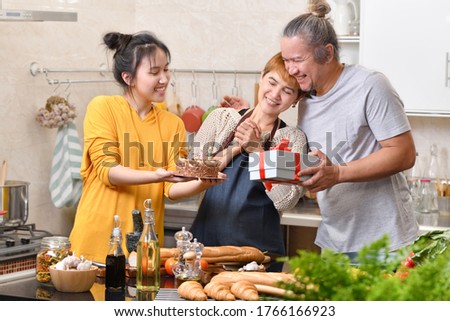 Happy family of mother father and daughter in kitchen celebrating birthday party together with cake and present