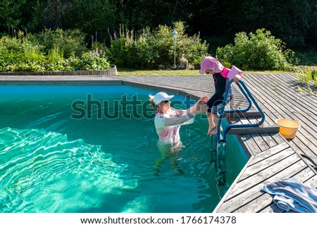 A girl, Caucasian, with a child girl 4 years old, swimming in the pool outdoors.