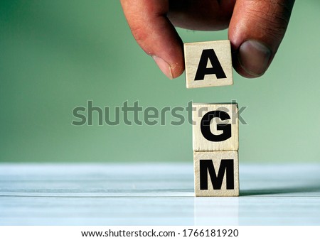 The hand puts the cube block with the inscription AGM. Annual general meeting - acronym on wooden cubes Royalty-Free Stock Photo #1766181920