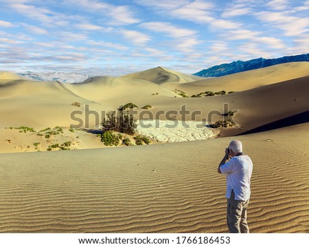  Sunset. Gray-haired man - tourist in T-shirt photographs magnificent landscape. Mesquite Flat Sand Dunes, Death Valley, California. USA. Concept of active and photo tourism