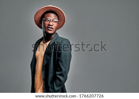 Isolated shot of fashionable serious young African American male in sunglasses, trendy hat and casual jacket , looks aside, isolated over gray studio background. People and style concept. Copy space