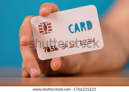 A closeup shot of a person holding a credit card paper cut-out on a blue blurry background