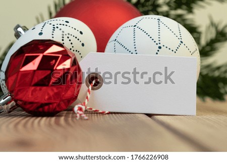 A closeup of colorful Christmas ball ornaments with a small blank wish tag on the table under the lights