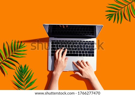 Person using a laptop computer with tropical leaves from above