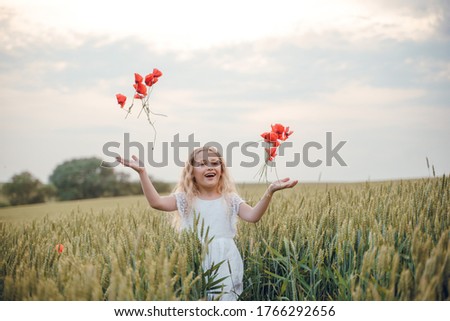 beautiful little girl with blond hair in a white dress in the background of a beautiful field. Girl with a bouquet of red poppies