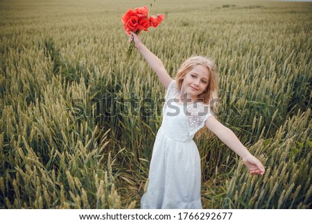 beautiful little girl with blond hair in a white dress in the background of a beautiful field. Girl with a bouquet of red poppies