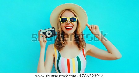 Summer portrait happy smiling young woman with retro camera wearing a summer straw hat on blue background