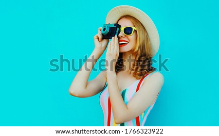 Summer portrait happy smiling young woman with retro camera wearing a summer straw hat on blue background