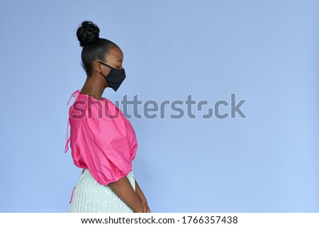 Young adult african american woman wearing stylish trendy fashion clothes and black cotton designed medical face mask standing isolated on lilac violet mauve studio background. Coronavirus protection. Royalty-Free Stock Photo #1766357438