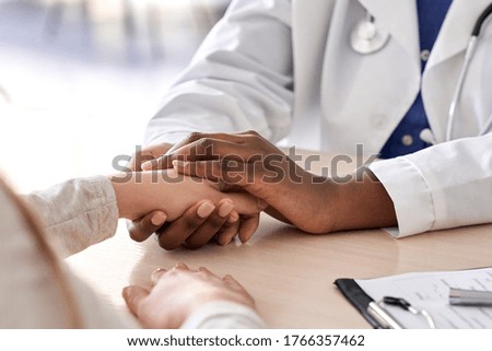 African female doctor hold hand of caucasian woman patient give comfort, express health care sympathy, medical help trust support encourage reassure infertile patient at medical visit, closeup view.