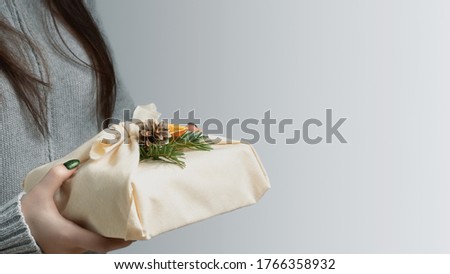 Zero waste and eco friendly christmas concept. Young woman holding in her hands a gift wrapped in natural fabric and decorated with natural materials