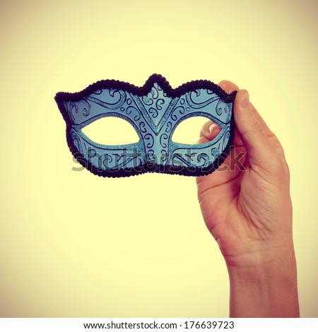 picture of a man hand holding a blue carnival mask on a beige background, with a retro effect
