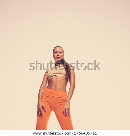 Portrait of beautiful young healthy woman in sportswear posing on studio toned background