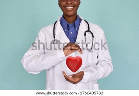 Smiling African female doctor wear white lab coat, stethoscope holding red heart in hands. Cardiology healthcare, love medicine charity, healthy heart protection, cardiac diseases concept, close up. Royalty-Free Stock Photo #1766405783
