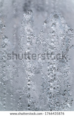 Splashes of water against light background. Fountain, a jet of water against cloudy sky.