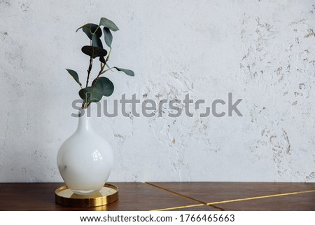 A cherry branch with green leaves stands in a white frosted round vase. The vase sits on a wooden table next to a white loft-style wall. High quality photo